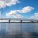 A long bridge stretches across a large body of water in front of a hillside